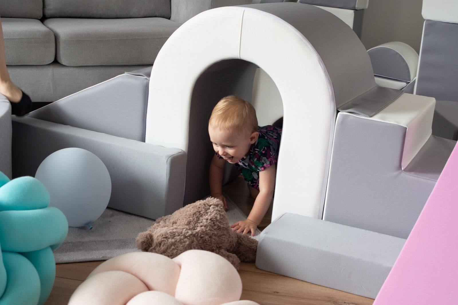 En lille pige smiler imens hun kravler gennem skumlegetøjets bro